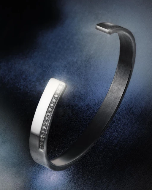 Silver open bangle bracelet with diamond accents on a textured dark blue backdrop for jewellery advertising and fashion accessories.