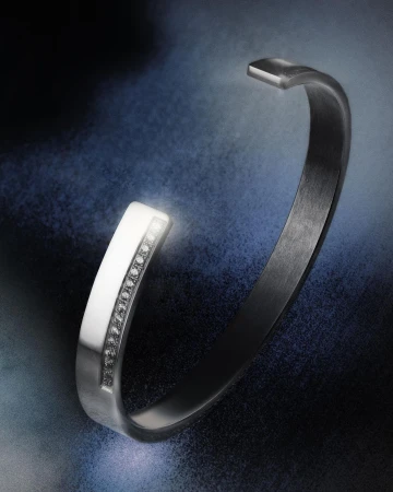 Silver open bangle bracelet with diamond accents on a textured dark blue backdrop for jewellery advertising and fashion accessories.