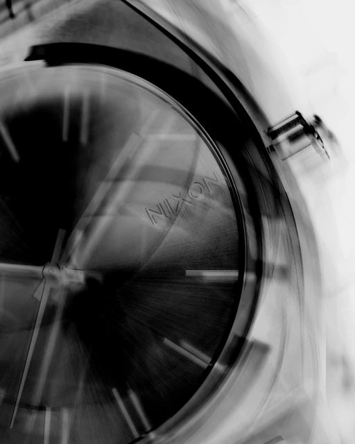 Monochrome image of a Nixon wristwatch close-up, focusing on the dial and hands, with blurred motion and a high-contrast, abstract aesthetic.