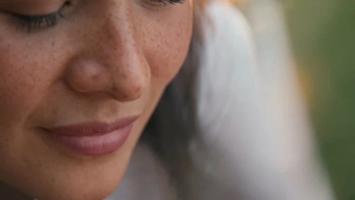 Close-up portrait of a woman's face highlighting visible freckles across her nose and cheeks with soft natural lighting