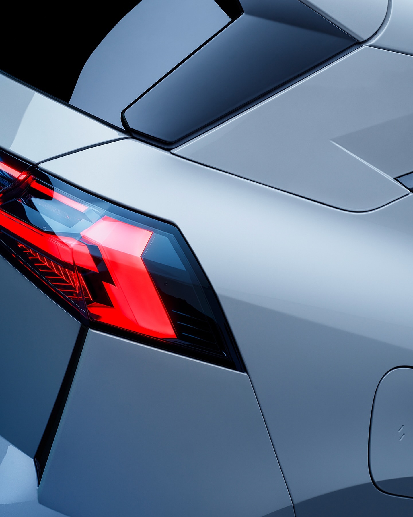 Close-up shot of a modern silver car's taillight and rear spoiler against a black background, showcasing automotive design details.