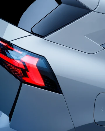 Close-up shot of a modern silver car's taillight and rear spoiler against a black background, showcasing automotive design details.