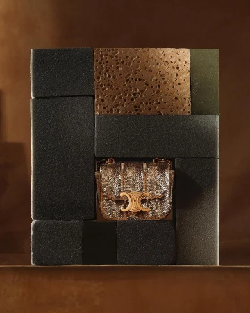 Studio shot of a gold sequined handbag with a gold metal logo, displayed within an arrangement of dark gray blocks.