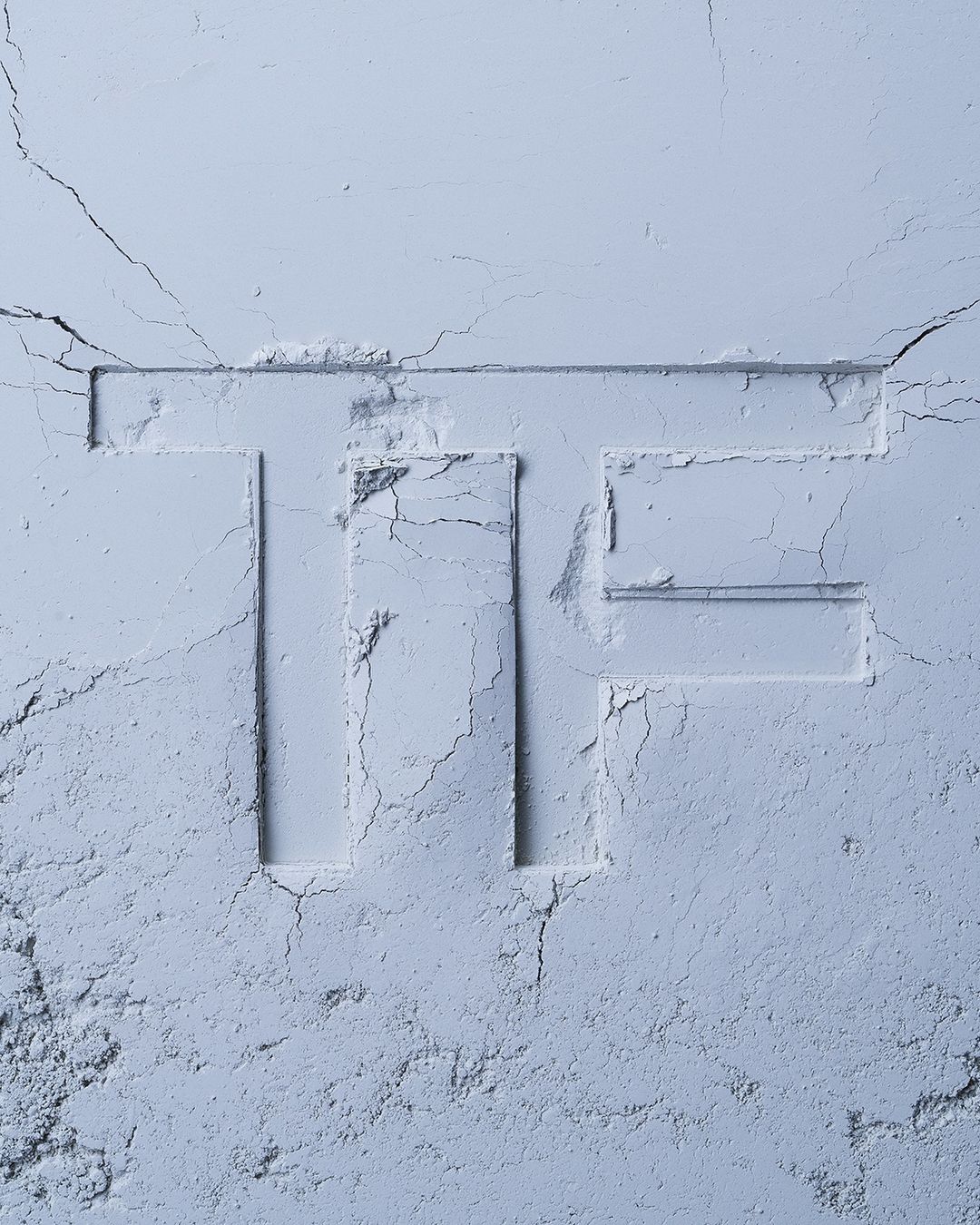 Monochromatic close-up of light blue cosmetic powder, with the letter 'TF' imprinted. Soft texture and subtle shadows create a gentle aesthetic.