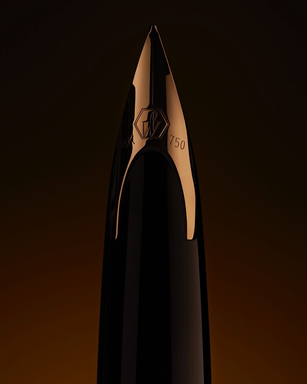 Close-up shot of a fountain pen nib with the number 750. The nib is partially gold and black. Brown gradient background.