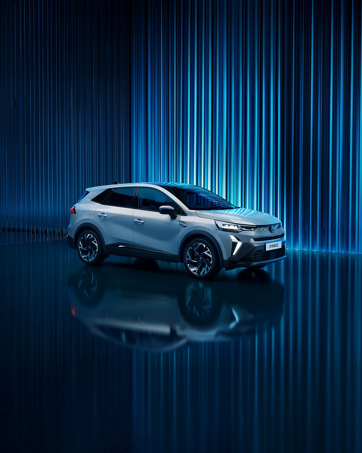 Sleek silver SUV parked indoors with dynamic blue lighting reflecting on a glossy surface, showcasing modern automotive design and technology.