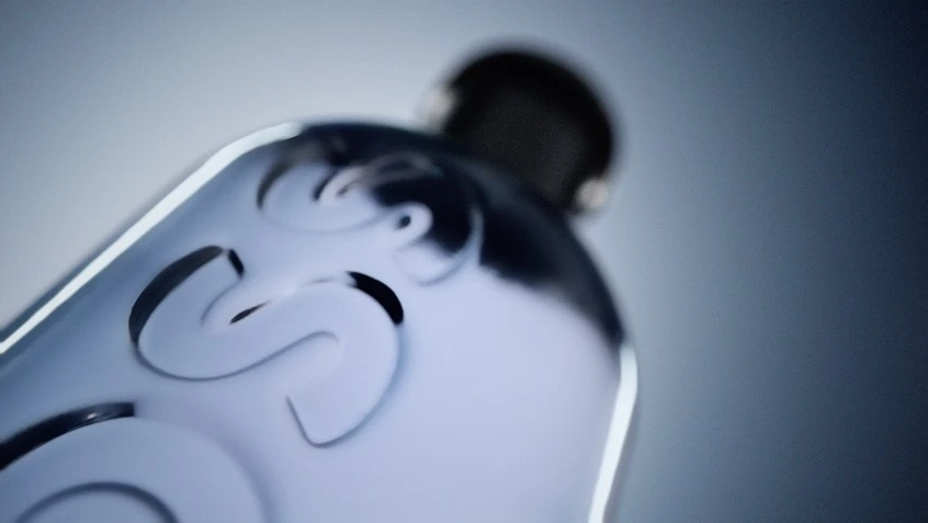 Close-up of a glass perfume bottle featuring carved letters, illuminated by studio lighting against a gradient blue and white background.