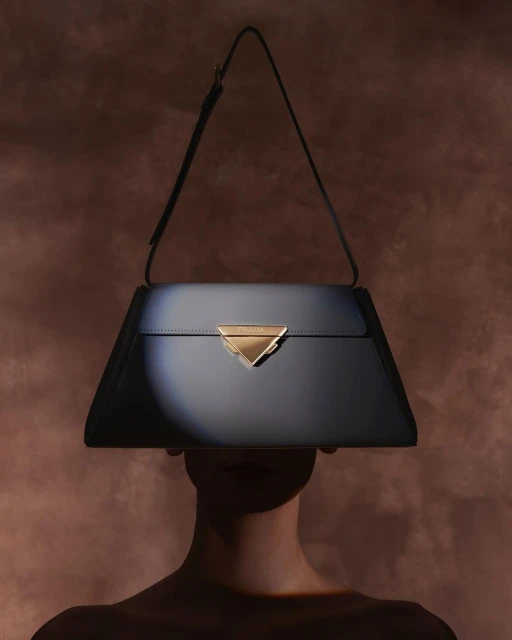 Fashion shot of a woman partially hidden behind a navy-blue trapezoid-shaped leather handbag with a triangular gold clasp.