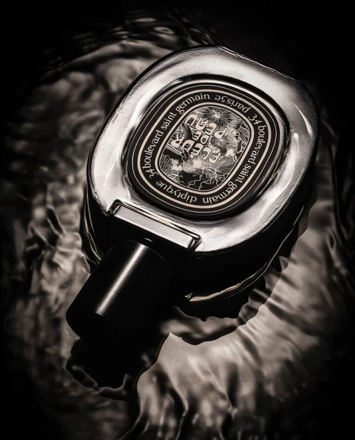 Close-up studio shot of a Diptyque perfume bottle on a water surface, featuring a monochrome palette and minimalistic design.
