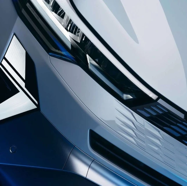 Close-up angled shot of a futuristic white and dark blue car hood with angular headlight design and glossy texture.
