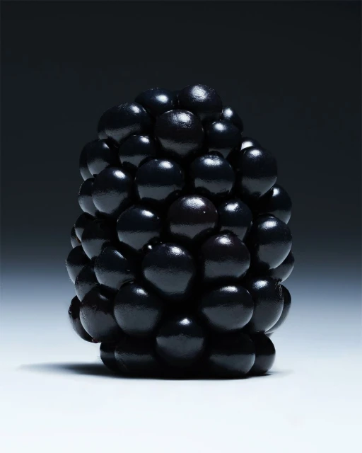 Close-up product photography showcases a single blackberry against a dark background, highlighting its dark purple color and textured surface.