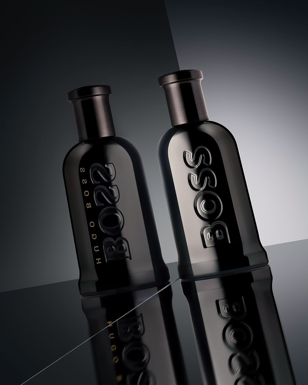 Studio shot of two dark-tone Hugo Boss perfume bottles on a reflective black surface, showcasing their sleek design and branding.