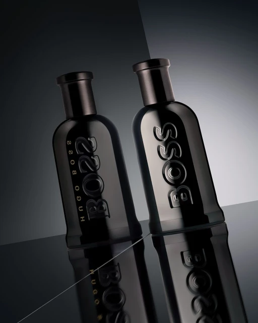 Studio shot of two dark-tone Hugo Boss perfume bottles on a reflective black surface, showcasing their sleek design and branding.