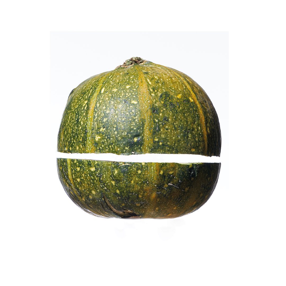 Studio shot of sliced kabocha squash against a white background with natural light, showcasing its green rind and orange flesh.
