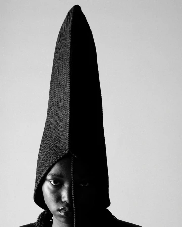 Portrait of a person wearing a tall pointed black knit hood against a light background by Akatre.
