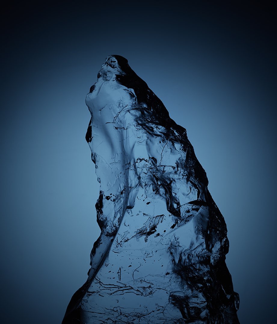 Translucent blue ice or glass chunk against a gradient blue backdrop, presenting an abstract and cold-toned visual texture.
