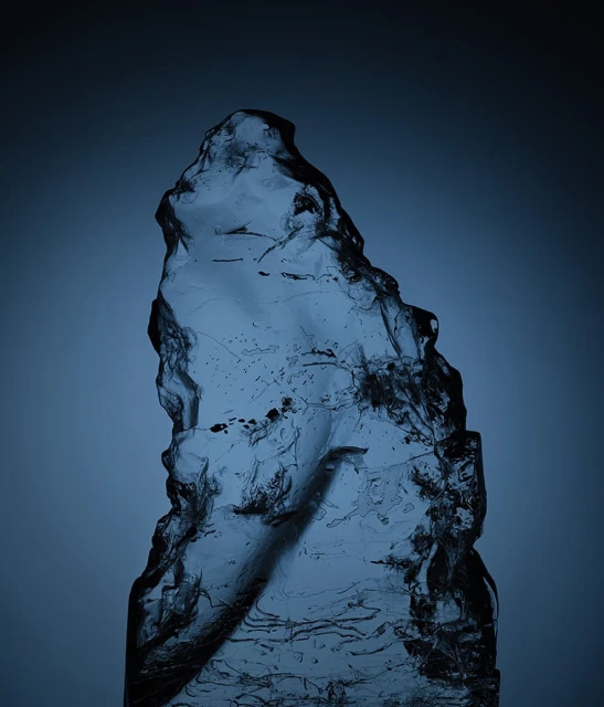 Abstract studio shot of a translucent icy shard with a rippled surface, set against a gradient dark blue background.