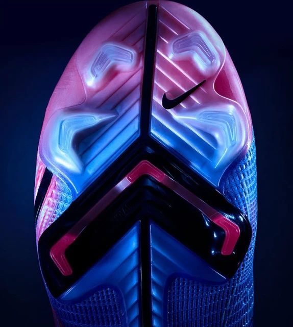 Close-up of the sole of a blue and pink Nike soccer cleat, showing the studs and Nike logo on a dark background.