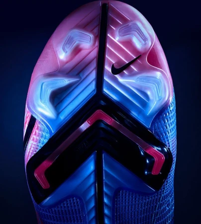 Close-up of the sole of a blue and pink Nike soccer cleat, showing the studs and Nike logo on a dark background.