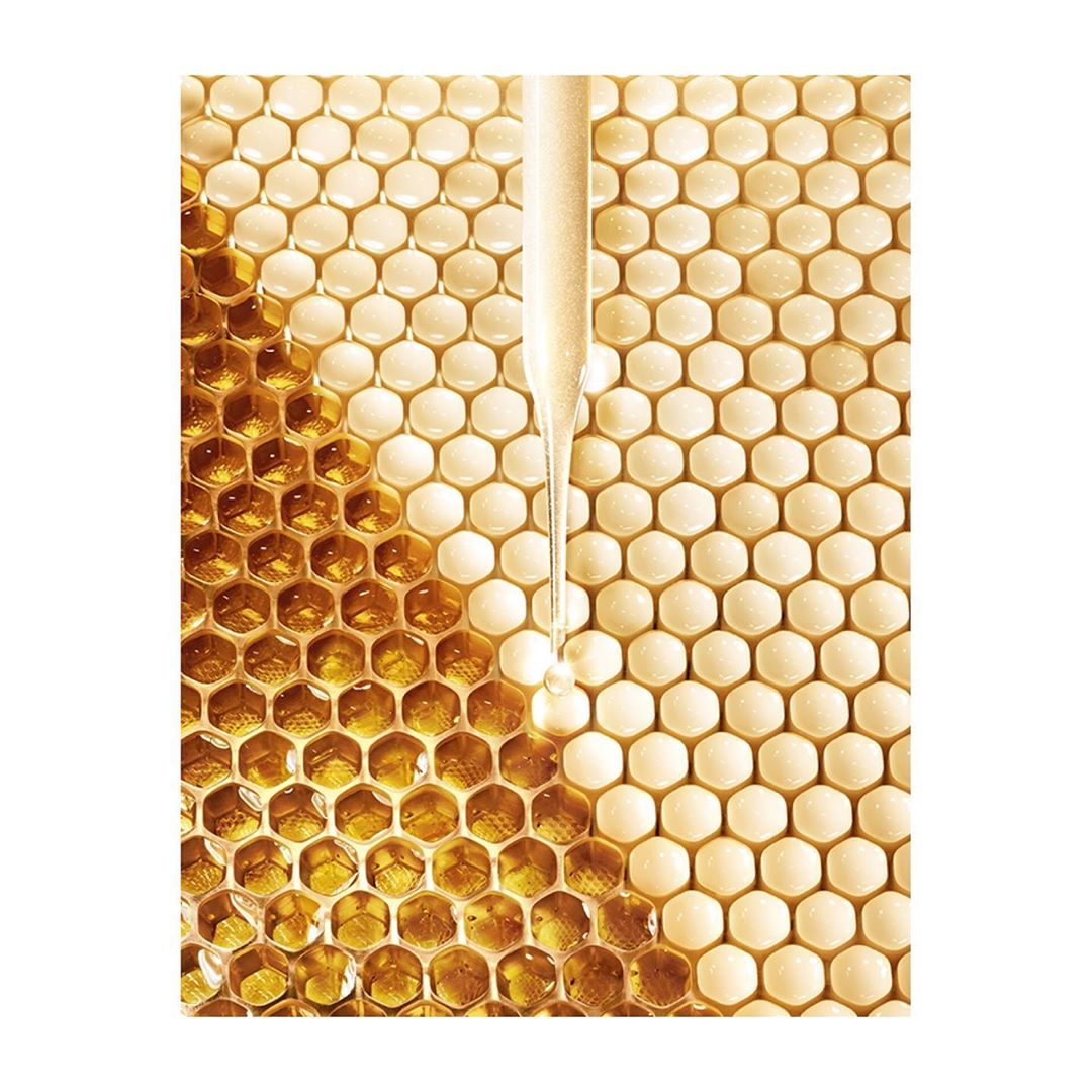 Close-up product shot: golden serum dripping from pipette onto light yellow honeycomb background. Beauty and wellness product photography.