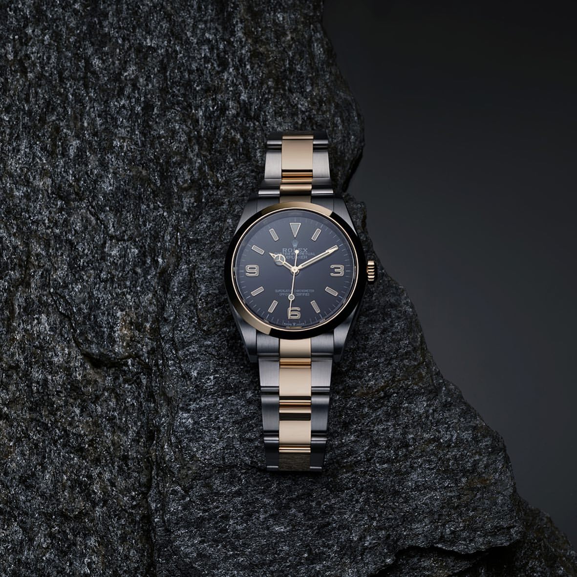 Close-up of a two-tone wristwatch with a black dial and silver and gold band resting on a textured grey rock surface.