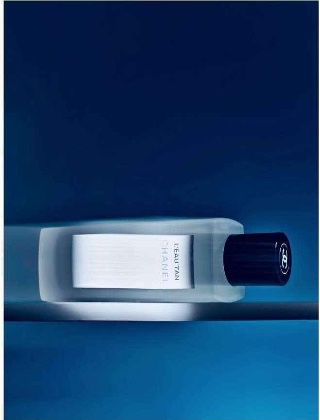 Chanel L'Eau Tan product shot against a blue background. Sleek white and clear bottle design with a black cap. Product shot.