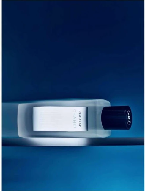 Chanel L'Eau Tan product shot against a blue background. Sleek white and clear bottle design with a black cap. Product shot.