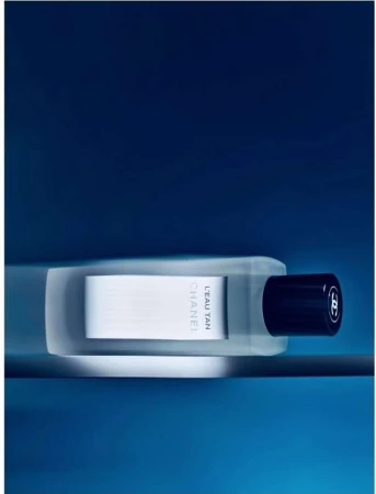 Chanel L'Eau Tan product shot against a blue background. Sleek white and clear bottle design with a black cap. Product shot.