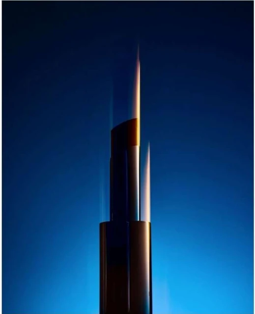 Abstract studio shot of a dark, cylindrical lipstick tube with a gold tip against a gradient blue background and dramatic lighting.