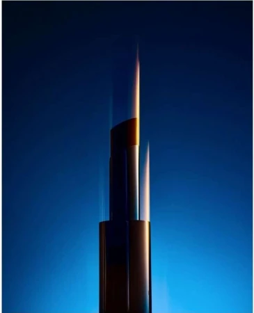 Vertical close-up of a lipstick tube lit with dramatic blue and amber lighting against a dark gradient background.
