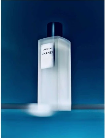 Frosted glass Chanel perfume bottle with black cap on reflective blue surface in a vertical portrait, beauty, fashion, luxury concept.