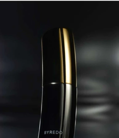 Close-up of a black Byredo perfume bottle with a gold cap against a blurred, dark background. Elegant presentation for beauty product.
