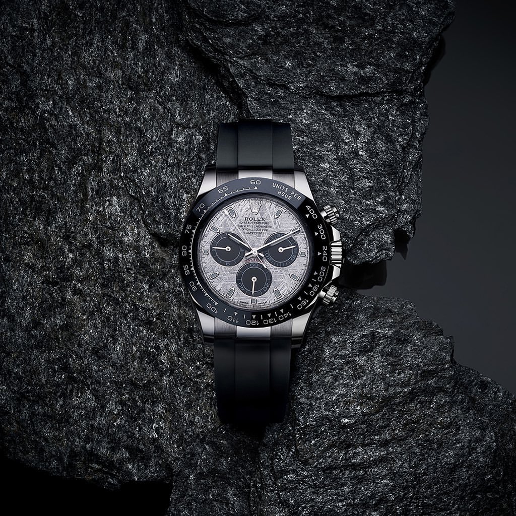 Elegant silver Rolex Daytona watch with black band and intricate dial, set on a textured dark gray rock surface.