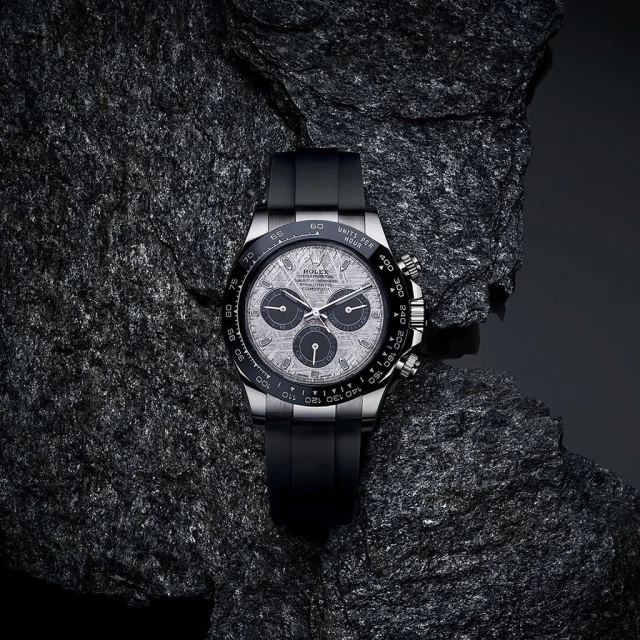 Elegant silver Rolex Daytona watch with black band and intricate dial, set on a textured dark gray rock surface.