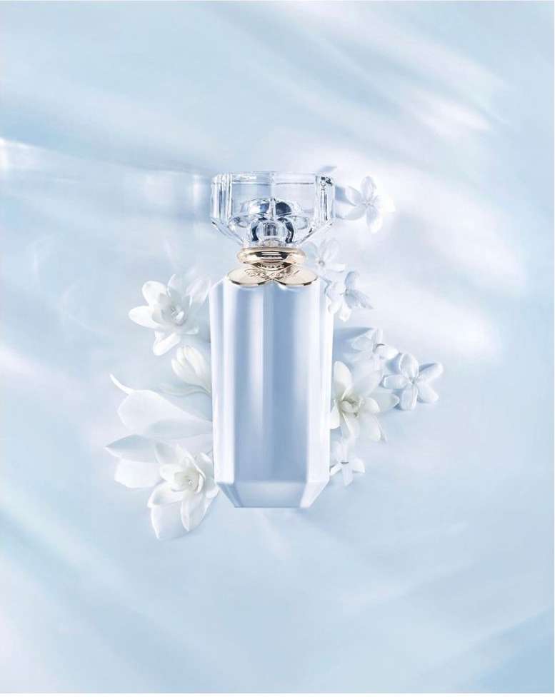 Elegant perfume bottle with a faceted glass cap and gold band, surrounded by delicate white floral accents against a soft blue backdrop.