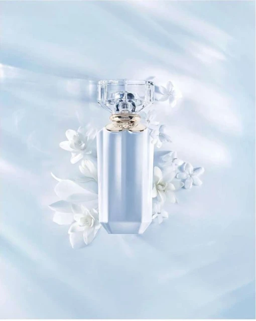 Elegant perfume bottle with a faceted glass cap and gold band, surrounded by delicate white floral accents against a soft blue backdrop.