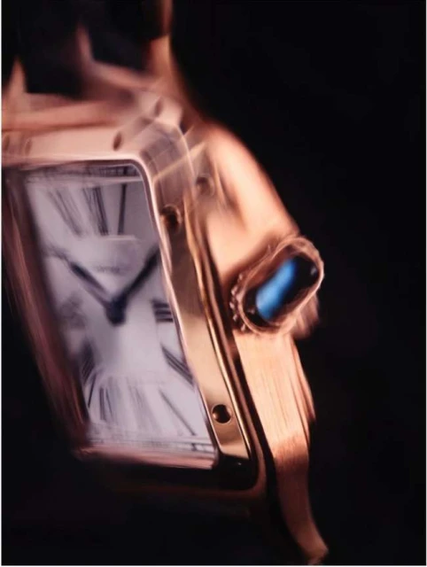 Rose gold wristwatch with a blue cabochon detail in a macro studio shot against a black background, showing the time on the watch face.