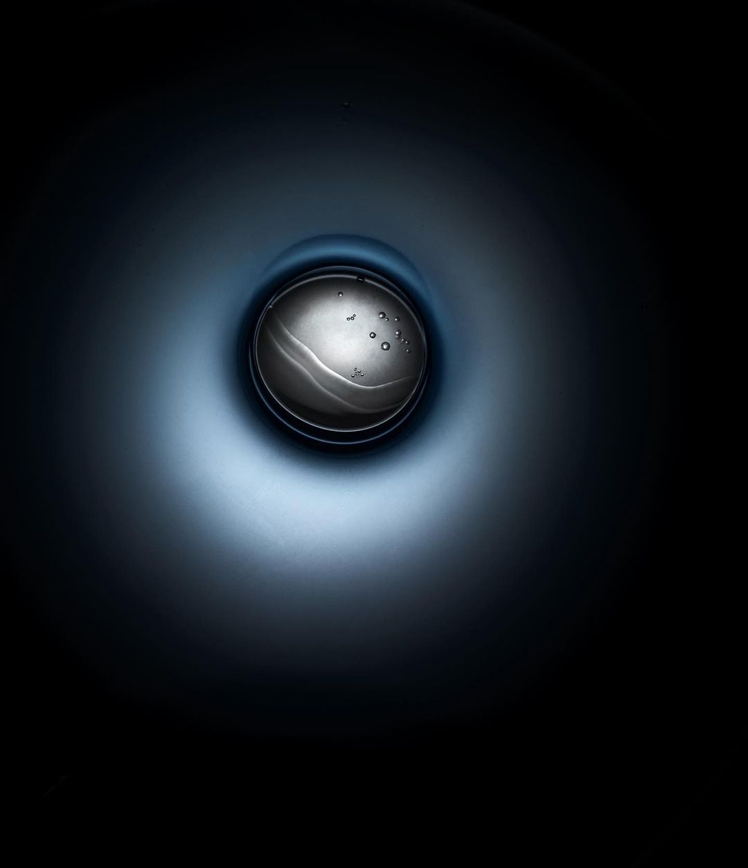 Abstract studio shot of an orb-like water droplet suspended in a dark blue gradient, creating a modern and minimalist visual.