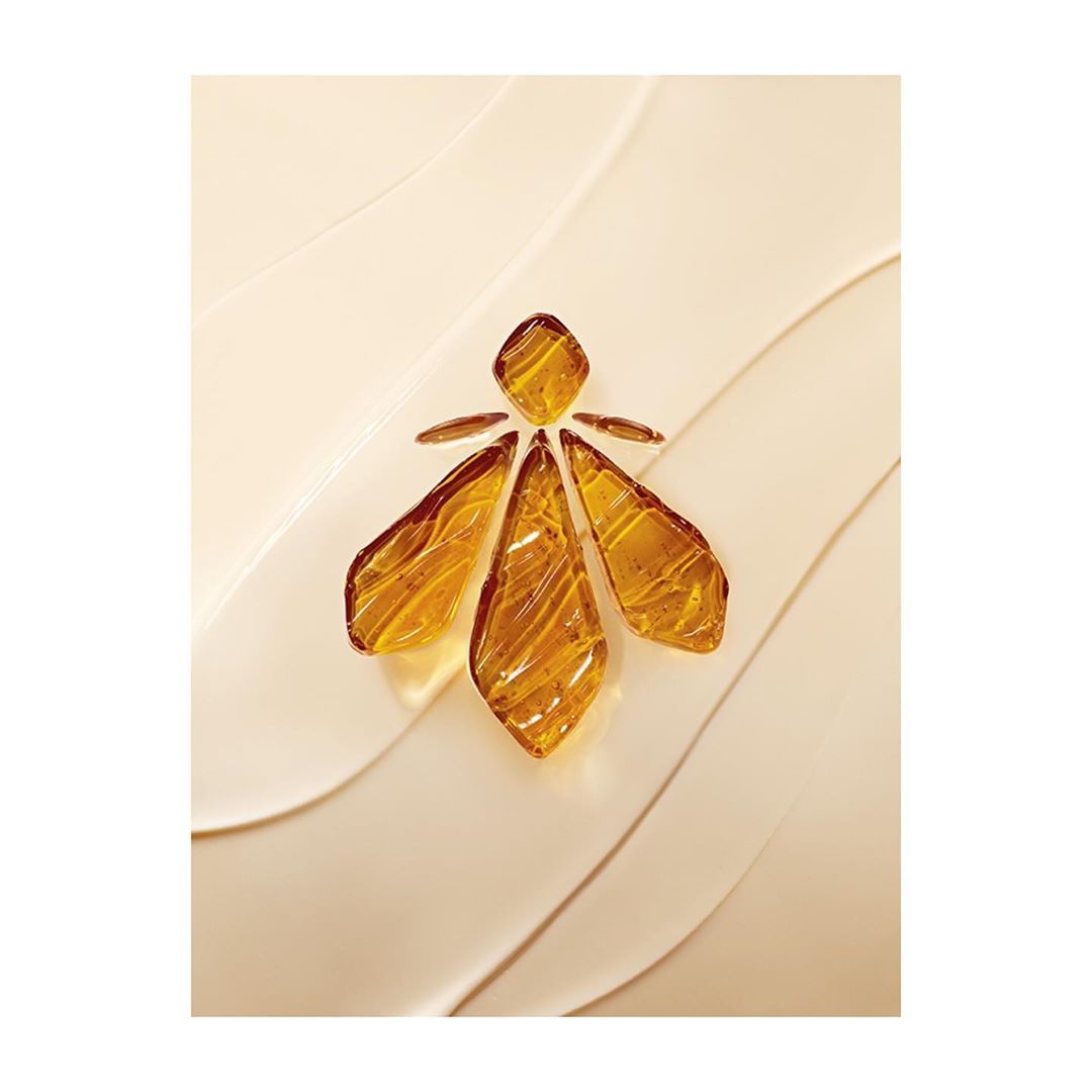 Close-up shot of an abstract bee-shaped design made of amber-colored pieces, set against a textured cream-colored background.