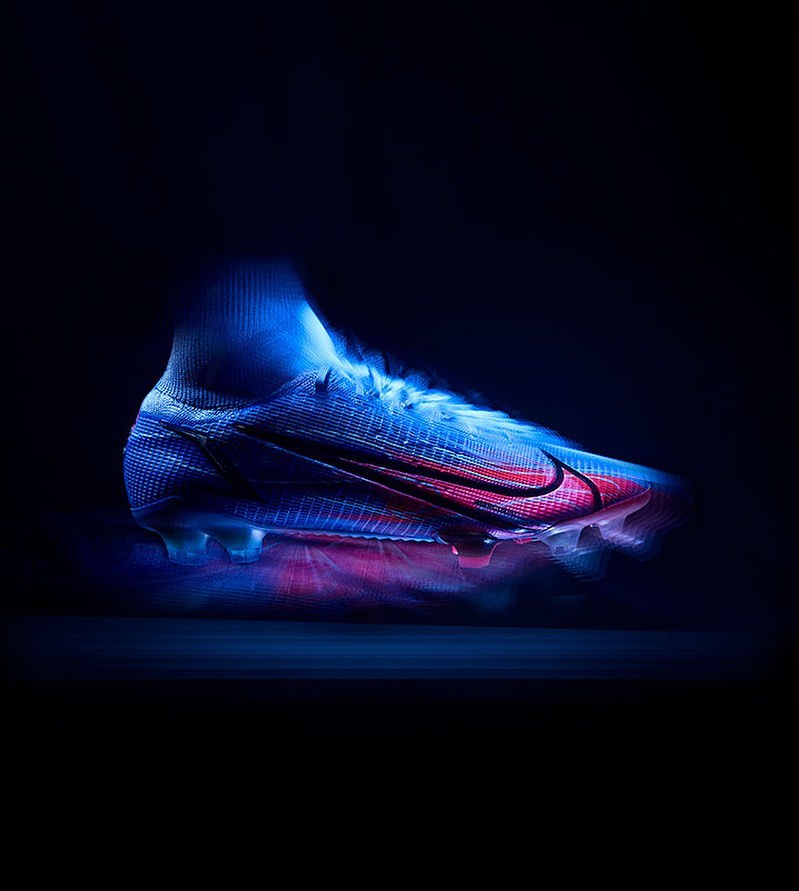 High-cut blue Nike Mercurial soccer cleat with a red swoosh logo against a dark background in a studio product shot. 