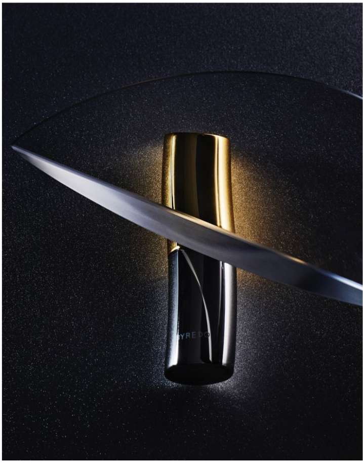 Byredo perfume bottle in black and gold with a blade on a dark surface. Studio shot emphasizes the bottle's design and luxury appeal.