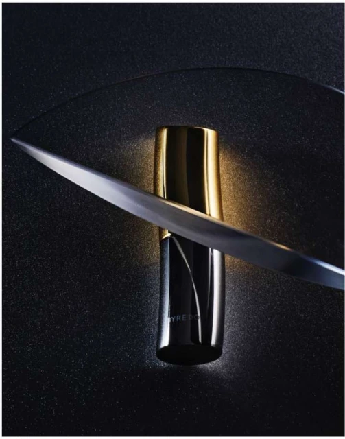 Byredo perfume bottle in black and gold with a blade on a dark surface. Studio shot emphasizes the bottle's design and luxury appeal.