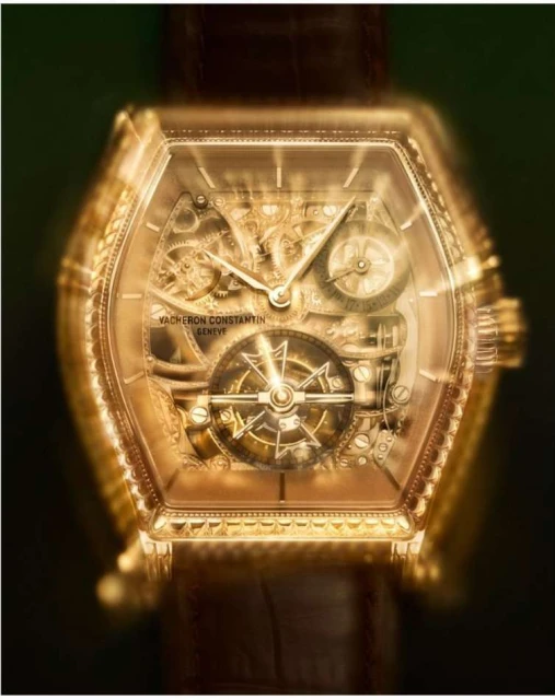 Close-up studio shot of a gold-toned Vacheron Constantin wristwatch with an ornate skeletonized face and brown leather strap against a dark backdrop.