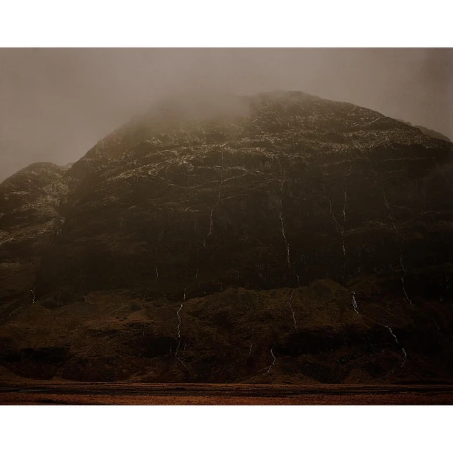 Cloudy mountain peak with visible streams running down its rocky face in a low-angle shot, creating a dramatic and isolated scene.