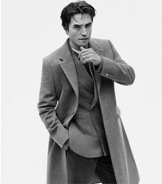 Black and white portrait of a man in a grey overcoat and suit against a white background. Fashion photography with a shallow depth of field.