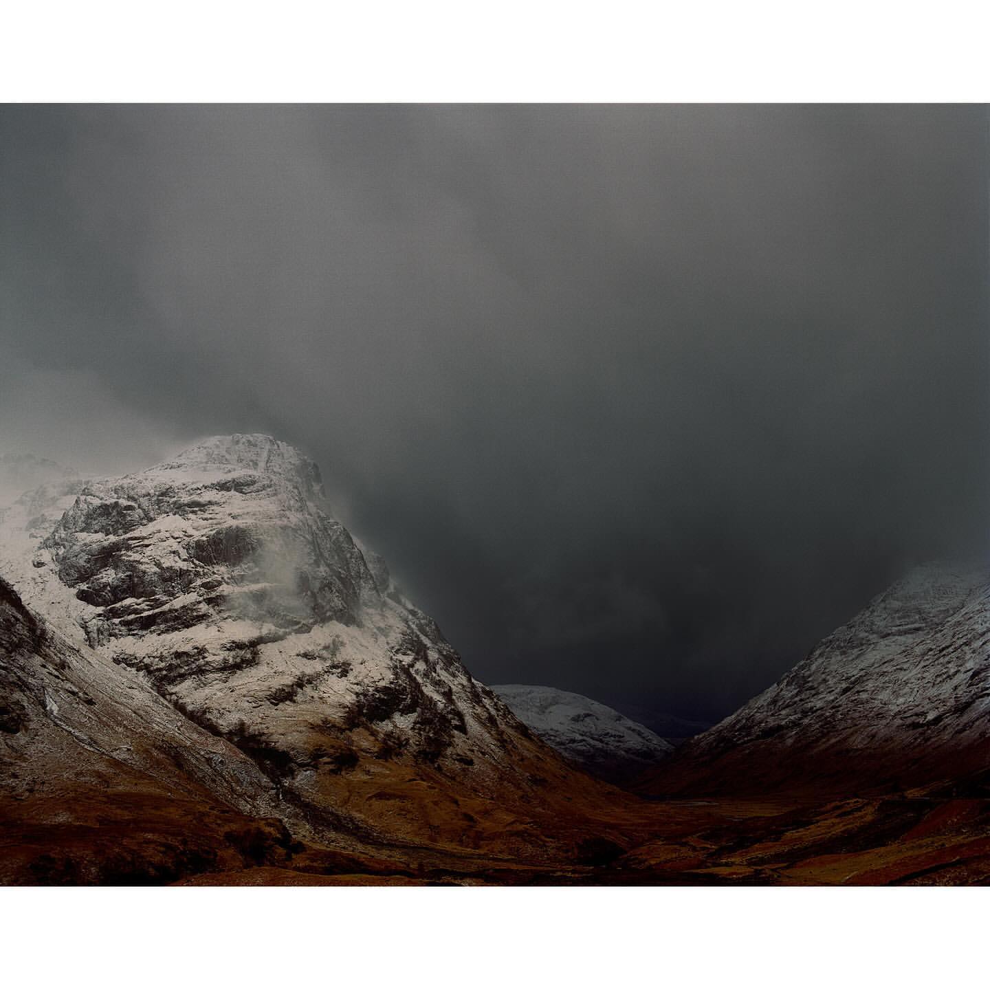 Snow-dusted mountains under an overcast sky, featuring a valley in a remote, cold climate, creating a somber and dramatic scene.
