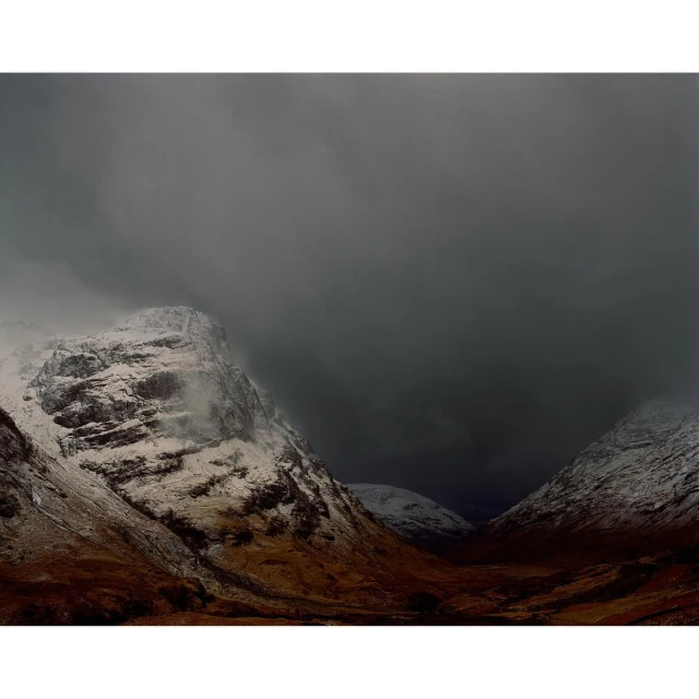 Snow-dusted mountains under an overcast sky, featuring a valley in a remote, cold climate, creating a somber and dramatic scene.