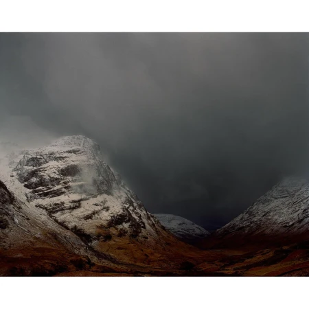 Snow-dusted mountains under an overcast sky, featuring a valley in a remote, cold climate, creating a somber and dramatic scene.