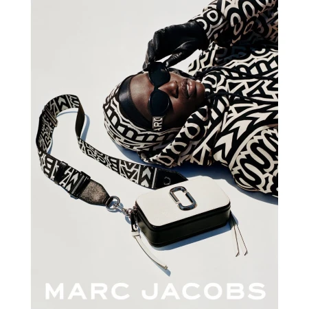 Model wearing black and white patterned hoodie and sunglasses with a white and black camera bag on a white background