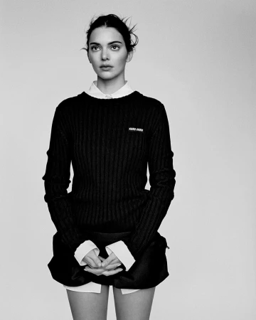 Kendall Jenner in a black ribbed sweater and white collared shirt against a seamless light background